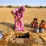 Indian woman drawing water from the well. Two of her children waiting for her - when she finish drawing water from the well, they together will carry water to the village. Rajasthani women and also children often walk long distances through the desert to bring back jugs of water that they carry on their heads . Thar Desert, Rajasthan. India.http://bem.2be.pl/IS/rajasthan_380.jpg